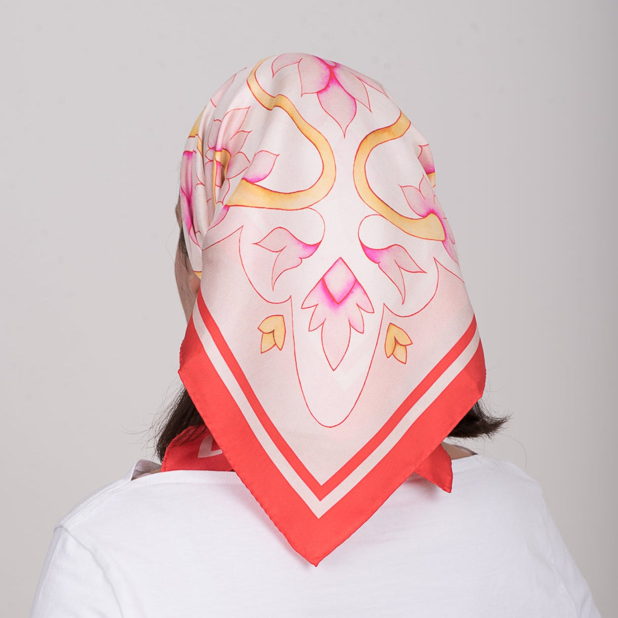 Person wearing a colorful headscarf with pink and red patterns on a plain background
