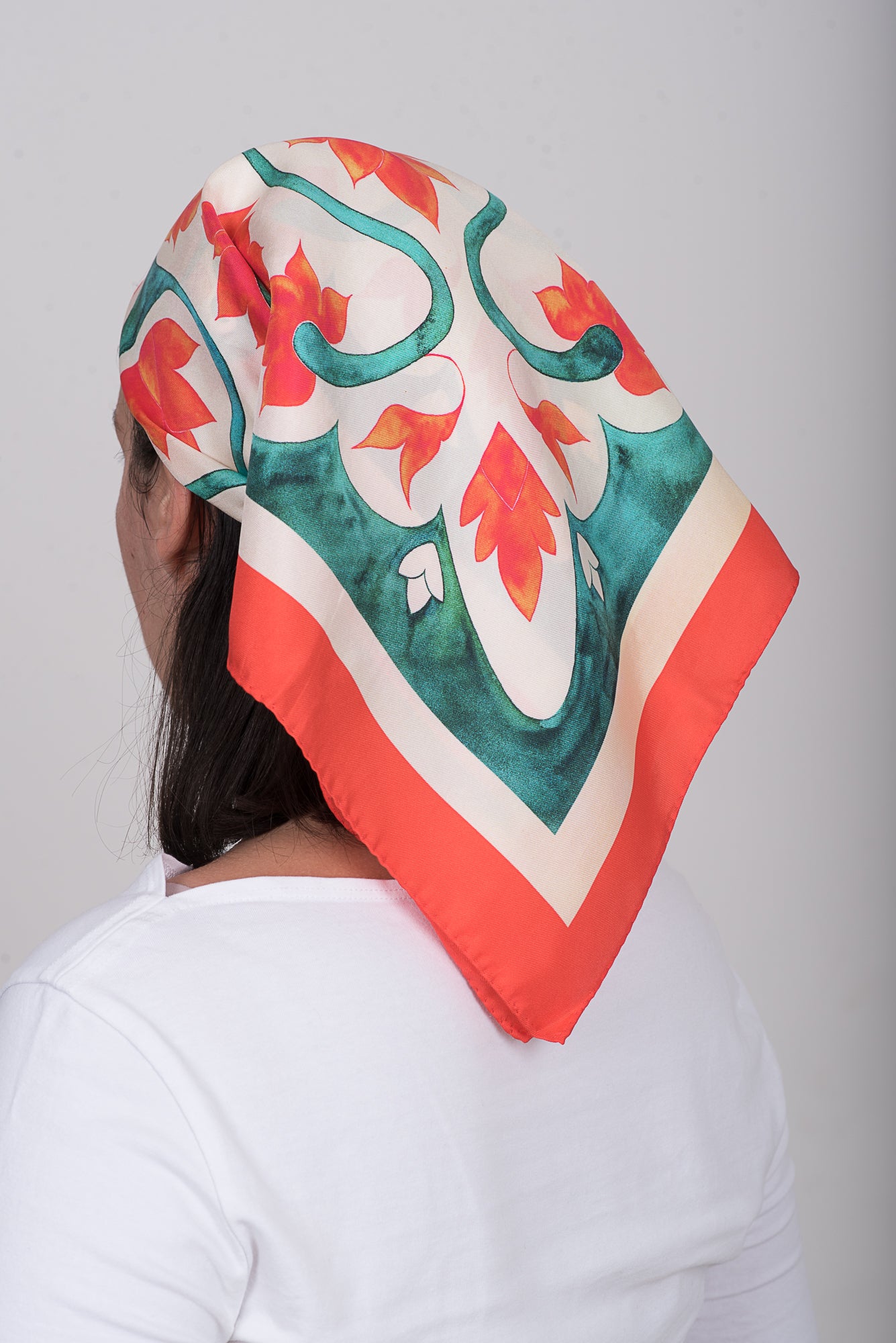 Square Greek folk art inspired silk scarf in teal and orange tones worn as headscarf