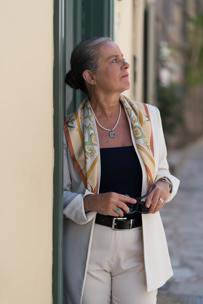Woman in a beige suit wearing Ariadne Kritonos' Cream Mesogeia Blooms scarf loosely on her back.