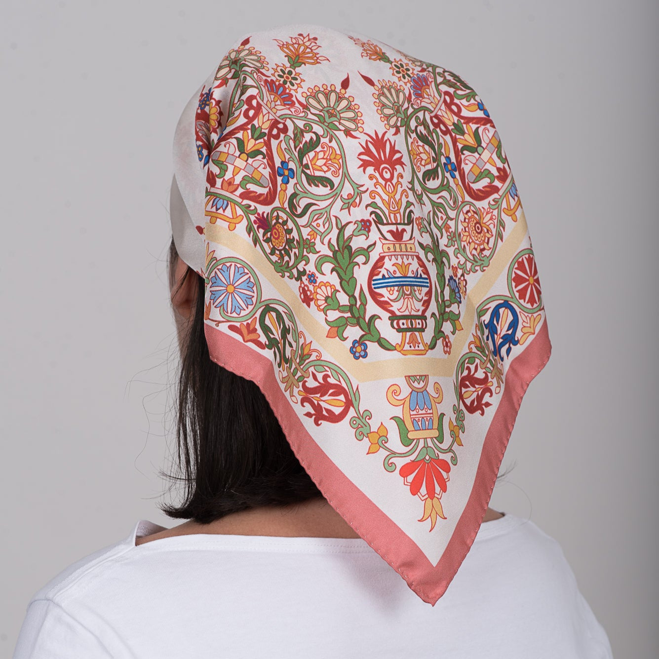 Greek folk art inspired square silk scarf in pink, red, cream and green tones worn as head wrap