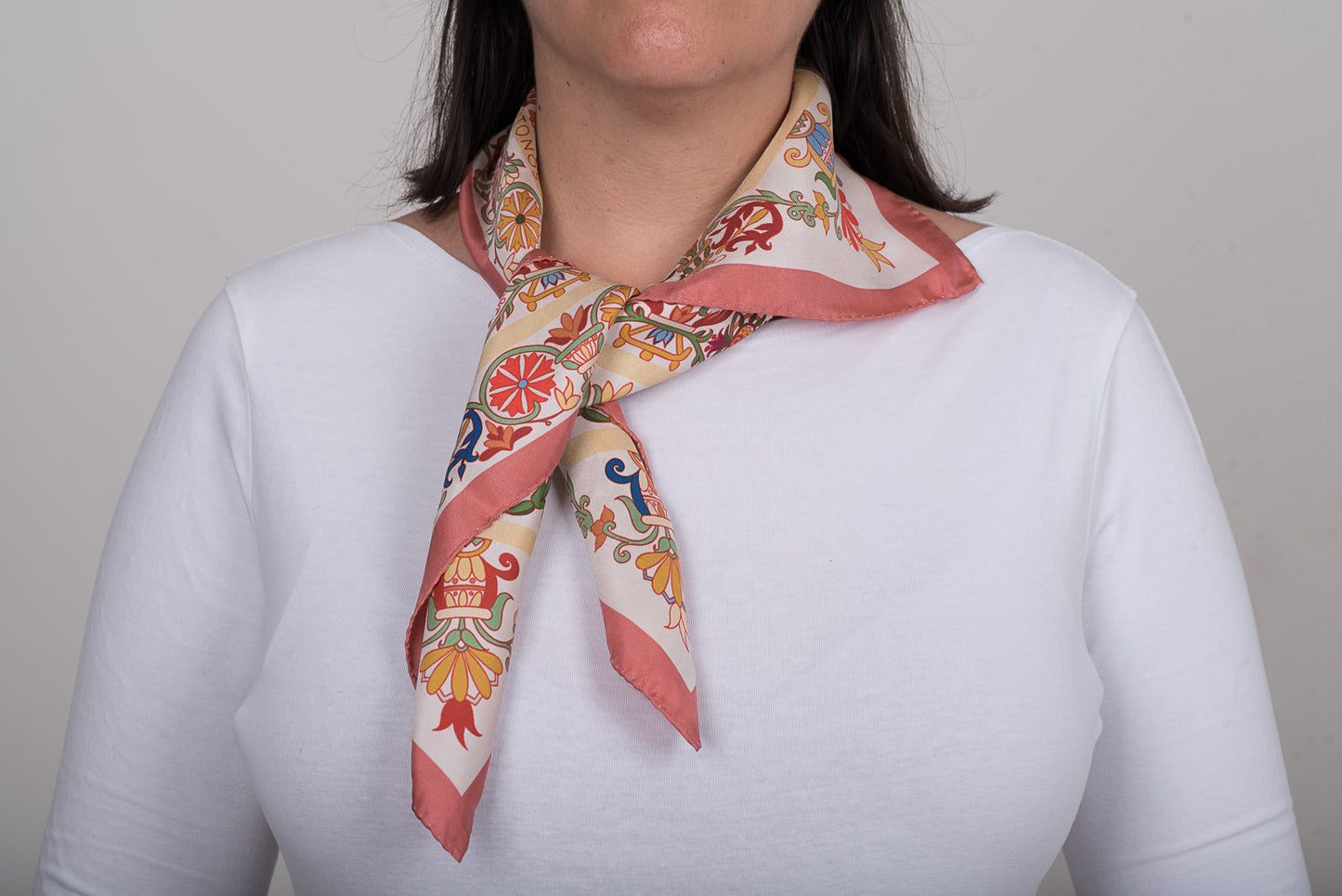 Woman wearing the colorfully patterned Cretan Mermaid silk scarf on a plain background