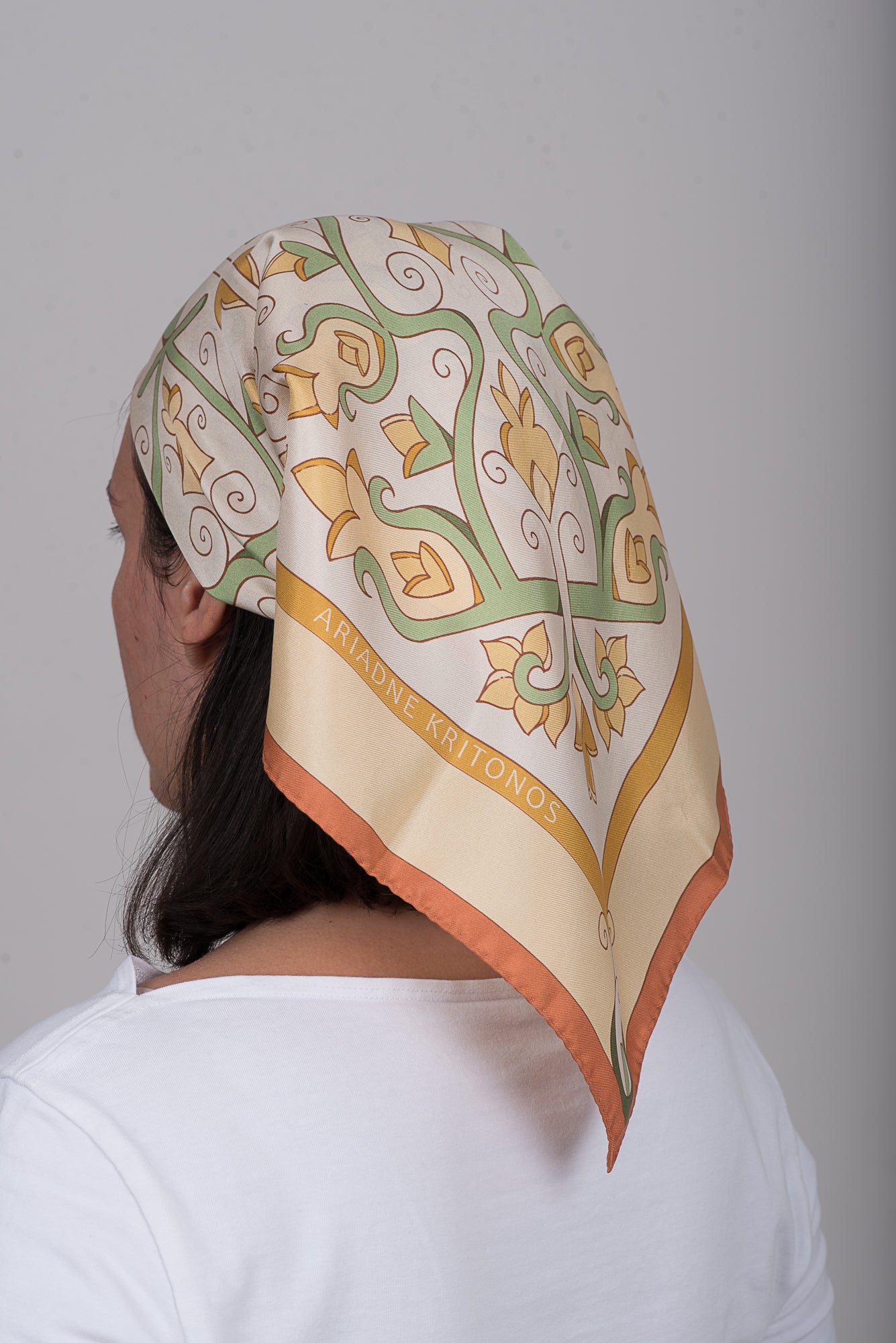 Silk Square scarf in cream, beige and pale yellow tones worn as head bandana with brand logo reading Ariadne Kritonos