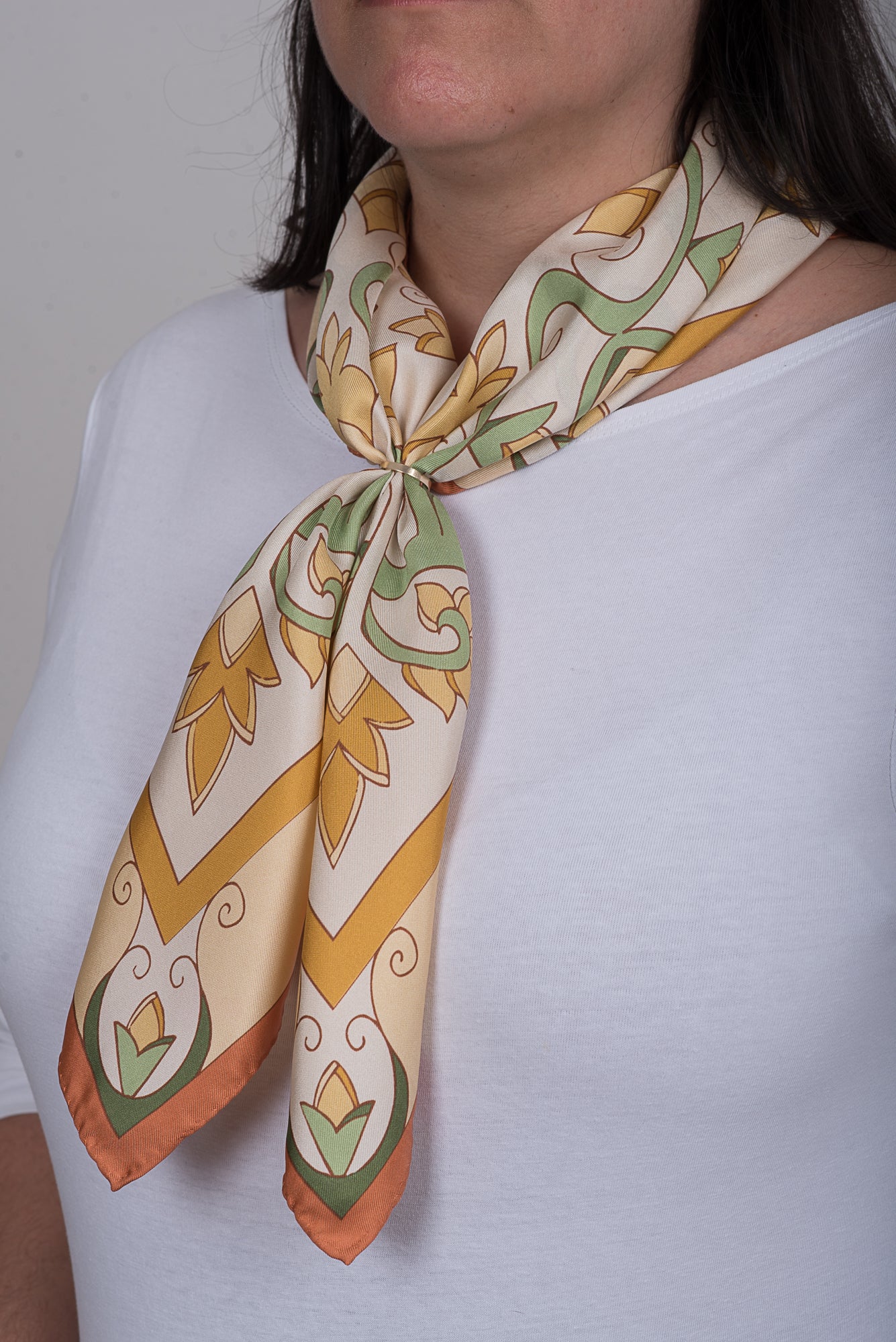 Close-up of cream Greek folk art inspired Mesogeia Blooms silk neckerchief held together with scarf ring.