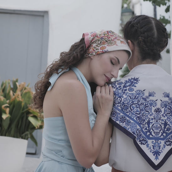 Close up video of model wearing blue Cretan mermaid silk scarf on her back
while another model rests her head on her shoulder and wears the pink version of the scarf.